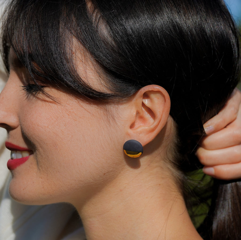 puces d’oreilles soleil en porcelaine noire et or portées à l'oreille